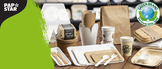 Eine Vielzahl von umweltfreundlichem Einweggeschirr, einschließlich Tellern, Bechern, Tabletts, Schachteln, Besteck und Tüten, aus Papier, Pappe und Holz. Das PAP STAR-Logo und die Plakette Green Brand Germany 2024/2025 sind sichtbar.