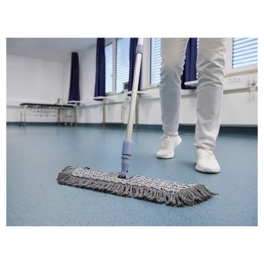 Eine Person in weißen Schuhen und Hosen wischt mit einem Vileda GmbH Professional Swep Duo r-MicroCombi Mop - 50 cm einen blauen Boden in einem Raum mit geschlossenen Jalousien und blauen Vorhängen. In der Nähe stehen ein Klapptisch und unter den Fenstern ein Heizkörper.