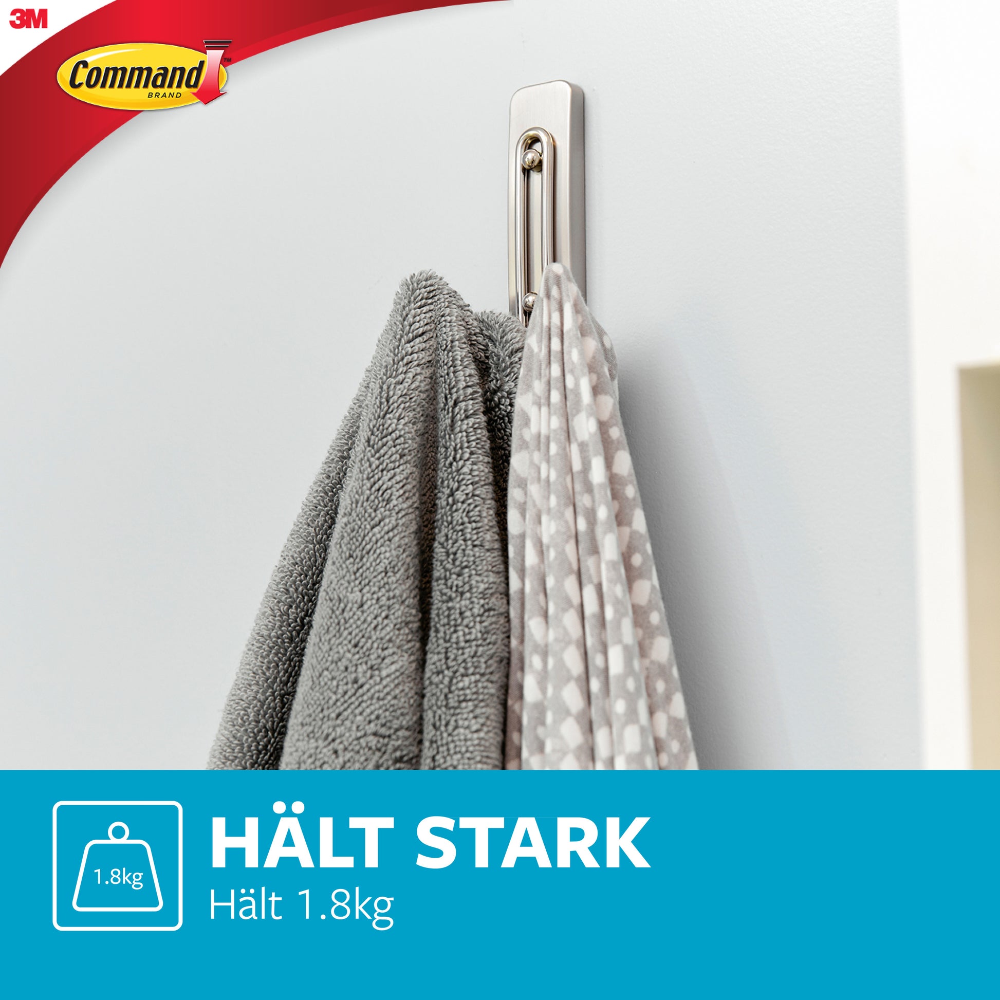A Command™ Großer Badezimmer-Doppelhaken Nickel satiniert von 3M Deutschland GmbH ist an einer weißen Wand montiert und hält ein graues Handtuch sowie ein weißes mit grauen Punkten. Text: "HÄLT STARK Hält 1,8kg", mit 3M-Logo in der Ecke.