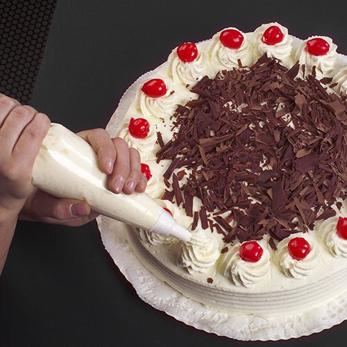 Met de Starpak 10 spuitzak 1,8 l met 3 spuitmondjes wordt een ronde taart gedecoreerd met opgespoten slagroom, chocoladeschaafsel in het midden en kersen bovenop, geplaatst op een witte taartdoily op een donkere ondergrond.