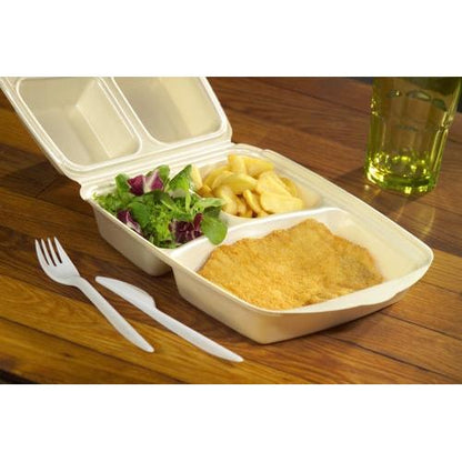 Een Starpak 50 menu box met klapdeksel, XPS beige gelamineerd, bevat een gepaneerde schnitzel, frietjes en groene salade. Ernaast liggen een plastic vork en een mes; op de achtergrond staat een geelgroene drank in een glas.
