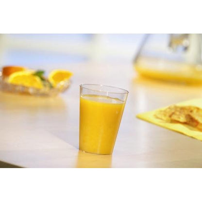 Un gobelet Starpak 40, PS 0,1 l Ø 5,5 cm · 7,5 cm transparent est rempli de jus d'orange sur une table claire. En arrière-plan, des tranches d'orange et une cruche - idéal pour les fêtes et événements.