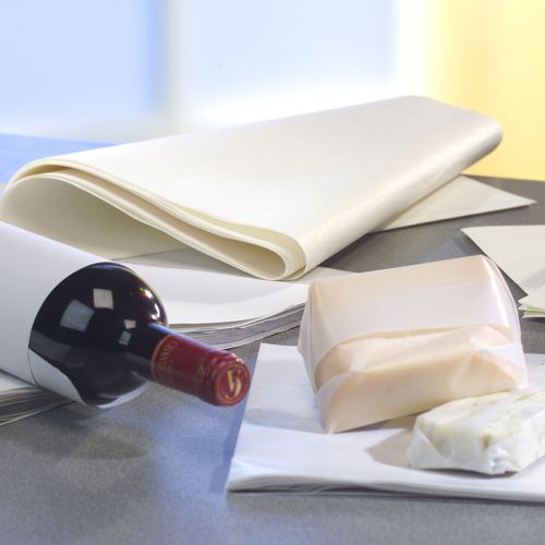 Une bouteille de vin est posée sur une surface grise, à côté PAPSTAR de papier cadeau de remplacement de parchemin « pur » blanc (12,5 kg, résistant à la graisse de la PAPSTAR GmbH) et de deux blocs de fromage, dont l'un est partiellement enveloppé. L'arrière-plan est légèrement flou.