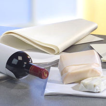 Une bouteille de vin est posée sur une surface grise, à côté PAPSTAR de papier cadeau de remplacement de parchemin « pur » blanc (12,5 kg, résistant à la graisse de la PAPSTAR GmbH) et de deux blocs de fromage, dont l'un est partiellement enveloppé. L'arrière-plan est légèrement flou.