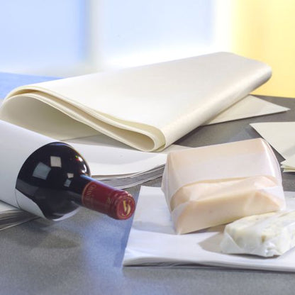 Une bouteille de vin est posée sur une surface grise, à côté PAPSTAR de papier cadeau de remplacement de parchemin « pur » blanc (12,5 kg, résistant à la graisse de la PAPSTAR GmbH) et de deux blocs de fromage, dont l'un est partiellement enveloppé. L'arrière-plan est légèrement flou.