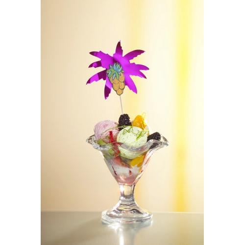Un bol à dessert en verre avec de la glace lumineuse, des fruits et des mûres est élégamment décoré avec un pique à cocktail "Feuilles de palmier" de 19,5 cm (assorti par couleur) de la PAPSTAR GmbH, provenant de l'ensemble de 50 pièces en plateau en carton, devant un fond jaune pâle.