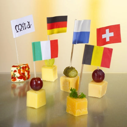 Six cubes de fromage, chacun surmonté d'un PAPSTAR 500 Deko-Picker 8 cm blanc de PAPSTAR GmbH. Certains cubes sont garnis de raisins, cornichons ou herbes. Le fond neutre, doucement éclairé, assure une présentation élégante.