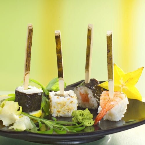Op een PAPSTAR kartonnen tray (200 stuks) liggen drie sushi-fingerfoods op PAPSTAR fingerfood-spiesjes (11 cm natuurlijk hout), vergezeld van stervrucht, wasabi, gember en groenten - perfect voor feestjes.