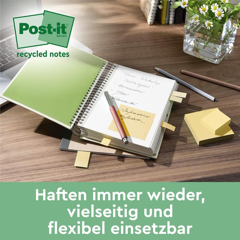 Een bureau met een spiraalnotitieboek met gele Post-it® Recycling Notes (76 mm x 76 mm, 100 vellen/blok, 100% PEFC) van 3M Deutschland GmbH, een pen, gestapelde plaknotities en een tablet. Op de achtergrond: een plant en de tekst "Haften immer wieder...