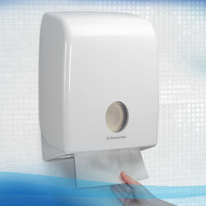 Une main tire une serviette Scott® ESSENTIAL™ de Kimberly-Clark GmbH d'un distributeur mural blanc dans des toilettes carrelées ; 15 paquets de 340 feuilles par carton.