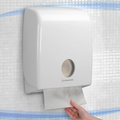 Une main tire une serviette en papier d'un distributeur mural blanc Aquarius™ pour serviettes pliées avec pliage en C de Kimberly-Clark GmbH, installé sur un mur carrelé.
