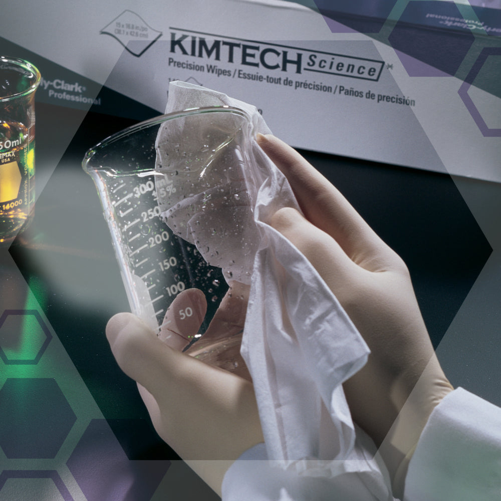 Eine behandschuhte Hand wischt ein Becherglas mit einem weißen Tuch neben einer Schachtel Kimtech® Science Präzisionstücher von Kimberly-Clark GmbH (Groß, Weiß, 15x196 Tücher) ab. Im Hintergrund sind Laborgeräte und andere Labortücher zu sehen.