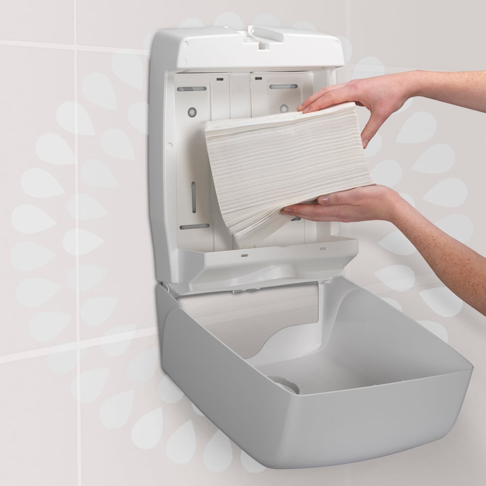 Een persoon laadt een stapel Kimberly-Clark GmbH Kleenex® Ultra™ Handdoeken MultiFold (Wit, Klein, 18 clips x 150 vellen) in een aan de muur gemonteerde papierhanddoekdispenser in een toilet.
