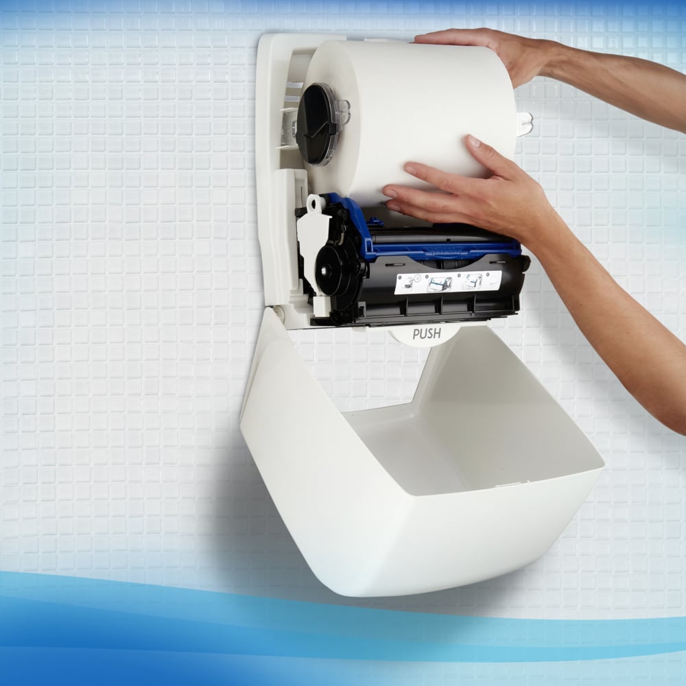Une personne installe une serviette Scott® Control™ - rouleau / blanc de Kimberly-Clark GmbH dans un distributeur mural sur un mur carrelé pour un séchage hygiénique des mains.