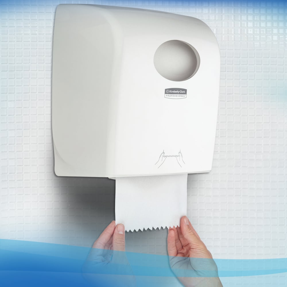 Une personne tire une serviette Scott® Control™ - rouleau / blanc d'un distributeur mural blanc de Kimberly-Clark GmbH dans une toilette avec des murs carrelés, assurant ainsi un séchage hygiénique des mains.