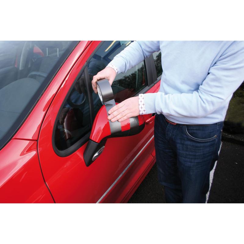 Une personne en pull bleu clair utilise le ruban adhésif en tissu haute performance Scotch® Extremium™ No Residue (18,2 m x 48 mm) de 3M pour fixer le rétroviseur latéral endommagé d'une voiture rouge, alors qu'elle se tient à la portière du conducteur. Le ruban gris est efficace et ne laisse pas de résidus.