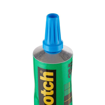 Gros plan d'un tube vert de 30 ml debout avec l'inscription "colle transparente sans solvant Scotch® pour la maison" de 3M Deutschland GmbH, avec un logo noir et jaune et un bouchon en plastique bleu.