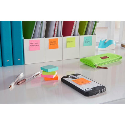 Een opgeruimd bureau met groene pennenzak, pennen, 3M Post-it® Super Sticky Notes (47,6 x 47,6 mm, 90 vel, 100% PEFC), een smartphone met een gelabelde notitie, mappen voor kantoormateriaal en rapporten en een blauwe plakbandhouder op de achtergrond.