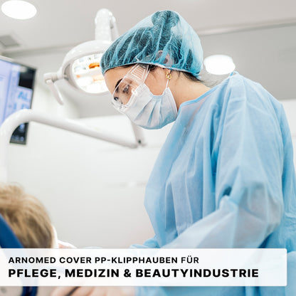 Un professionnel de la santé en EPI bleu examine un patient, à proximité d'appareils médicaux. Le texte fait la promotion du ARNOMED COVER PP-KLIPPHAUBE XL (55cm, non-tissé PP) de ARNOWA GmbH - la charlotte jetable idéale pour les secteurs des soins, de la médecine et de la cosmétique.
