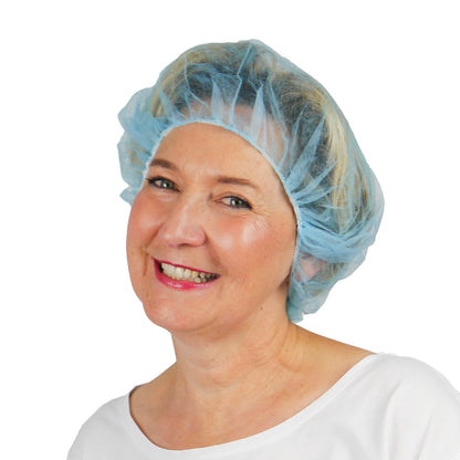Een vrouw in een lichtblauwe ARNOMED COVER PP-BARETTHAUBE baretkap van PP-vlies van ARNOWA GmbH en een wit bovenstuk glimlacht voor een eenvoudige witte achtergrond en benadrukt dit hygiënische accessoire voor de hygiënezone.