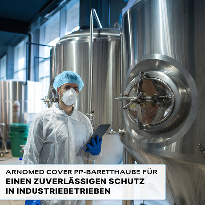 Een persoon die een ARNOMED COVER PP-BARETTHAUBE baretkap van PP-vlies van ARNOWA GmbH en een masker draagt, staat voor roestvrijstalen tanks in een industriële hygiënezone en houdt een tablet in de hand. De Duitse tekst benadrukt de betrouwbare bescherming voor de industrie.
