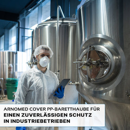 Een persoon in beschermende kleding, waaronder de ARNOMED COVER PP-BARETTHAUBE van ARNOWA GmbH en een masker, houdt een tablet naast roestvrijstalen tanks in een hygiënische industriële zone. De Duitse tekst over betrouwbare bescherming wordt onderaan weergegeven.