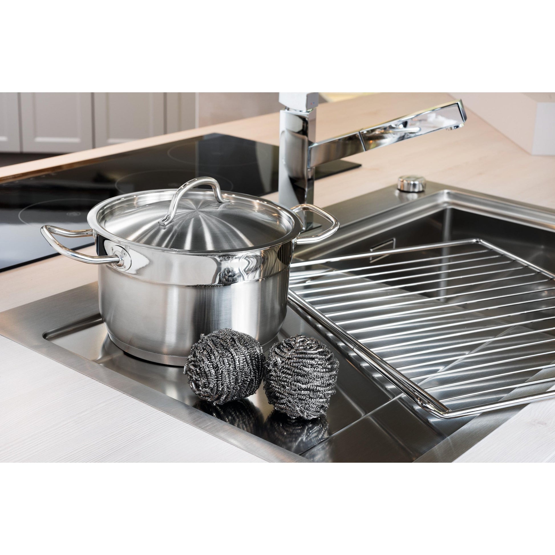 Auf der Küchentheke neben der Spüle steht ein Edelstahltopf mit Deckel neben einer Scotch-Brite® Edelstahl-Spirale der 3M Deutschland GmbH, die zu einem 3er-Pack gehört, sowie einem Metalltrockengestell und einem verchromten Wasserhahn im Hintergrund.