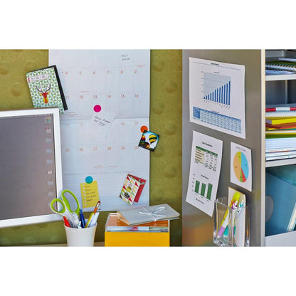 Un espace de travail avec un calendrier mural, des tableaux fixés avec les carrés de montage amovibles Scotch-FIX™ 108-ST64-P de 3M, un écran d'ordinateur, des dossiers colorés, une paire de ciseaux dans un support blanc, une boîte jaune et un pot de crayons. Les notes sont attachées avec ces tampons adhésifs sans résidus.
