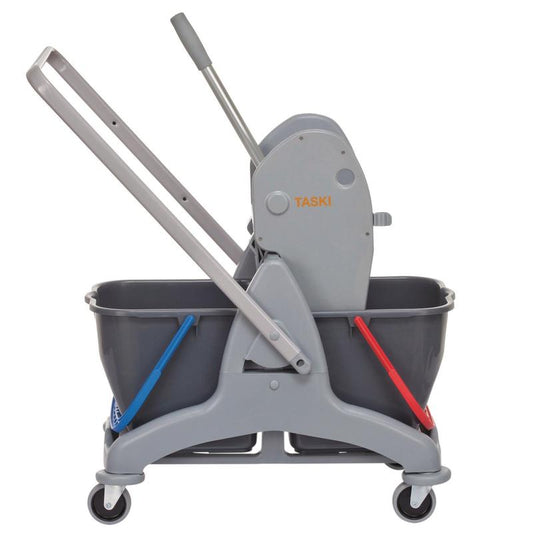 Ein graues TASKI Duo Mop Zweieimer-System von Diversey, mit zwei 15L Eimern (blau für sauberes, rot für schmutziges Wasser), vier Rädern, Griff und Presse - ideal für die hygienische Reinigung.