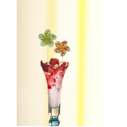 Un grand verre contient un dessert rose et blanc, surmonté de sauce à la fraise et d'un PAPSTAR pique décoratif "Moulin à vent" (17,5 cm, couleurs assorties), qui enrichit joyeusement la décoration de la fête. Le set de la société PAPSTAR GmbH contient 50 piques dans un plateau en carton.