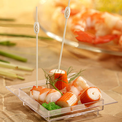Sur un plateau carré en plastique avec imitation de crabe, crevettes, œufs de poisson verts et garniture, deux PAPSTAR 40 pics à fingerfood « pure » de PAPSTAR GmbH sont illustrés, en arrière-plan, un plateau de fruits de mer similaire est visible de manière floue.
