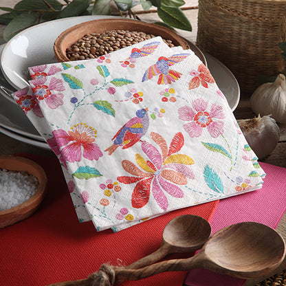 Une pile de PAPSTAR 20 serviettes, 25 x 25 cm, 3 plis, 1/4 pliage de la société PAPSTAR GmbH avec des motifs de fleurs et d'oiseaux colorés repose sur une table entre des cuillères en bois, des grains et un panier – parfaites pour une décoration de table vivante. En arrière-plan, des assiettes.