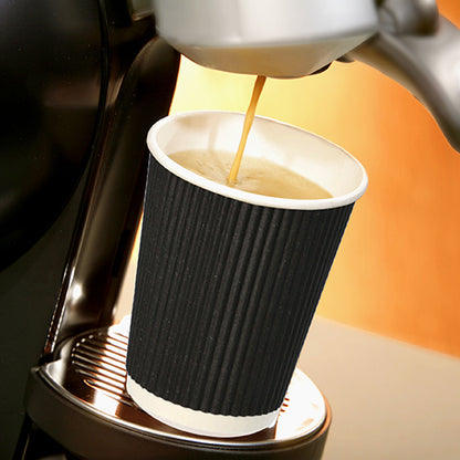 Un gobelet Starpak 25, carton "To Go" Ripple Wall se tient sur un plateau métallique sous le bec d'une machine à café, tandis que du café chaud y coule, se détachant sur un fond doucement éclairé aux tons chauds.