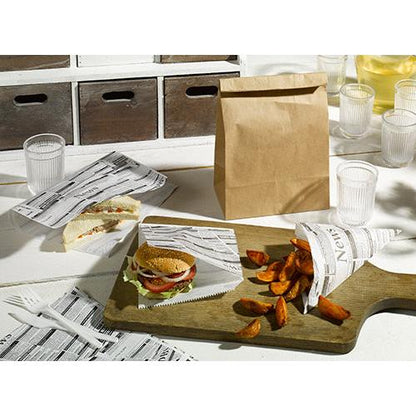 Sur une table recouverte de papier d'emballage substitut de parchemin 35x25 cm résistant à la graisse de la PAPSTAR GmbH sont servis un sandwich, un burger et des quartiers de pommes de terre, à côté se trouvent des gobelets transparents, un sac en papier brun, un pichet avec une boisson jaune et des couverts en plastique blanc.