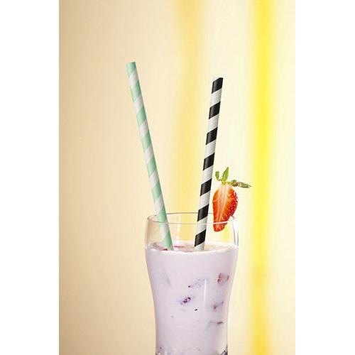 Dans un verre avec un milkshake rose, de la glace, des morceaux de fruits et une garniture à la fraise, se trouvent deux PAPSTAR 100 pailles en papier Ø 6 mm (de PAPSTAR GmbH), une à rayures vertes et une à rayures noires.