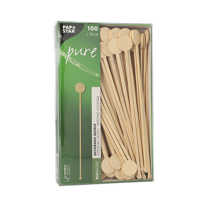 Een doos met 100 PAPSTAR GmbH 'pure' bamboe drankroerders, biologisch afbreekbaar, met ronde platte uiteinden, gedeeltelijk zichtbaar door een kijkvenster in groene en witte PAPSTAR Pure verpakking.