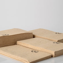 Vier Stapel PAPSTAR Servietten 3-lagig, 33x33 cm, natur, aus recyceltem Papier (100 Stück) von PAPSTAR GmbH liegen auf einer weißen Fläche. Jede recycelte Serviette ist in der Ecke mit einem kleinen schwarzen Recycling-Symbol versehen.