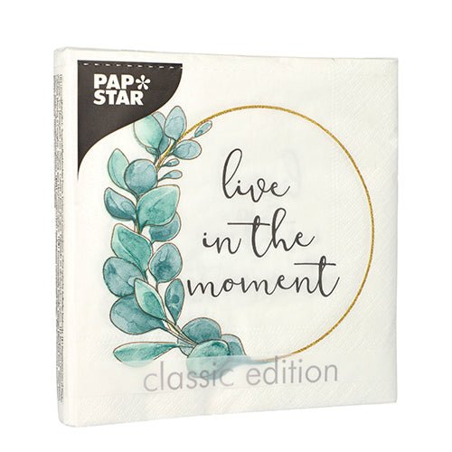 La serviette PAPSTAR GmbH 20 serviettes (33x33 cm, 3 plis, 1/4 pliées, Design Set 3) a un fond blanc avec des feuilles d'eucalyptus, un cercle doré et l'inscription "live in the moment". Logo PAP STAR en haut à gauche ; "classic edition" en bas.
