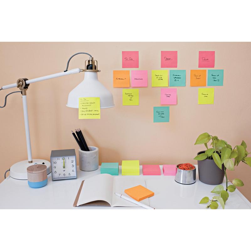 Een bureau met een witte lamp, potloden in een beker, een klok, een open notitieboek en een plant. De Post-it® Super Sticky Notes (47,6 mm x 47,6 mm) van 3M zijn met handgeschreven taken aan de beige muur boven het bureau gerangschikt.
