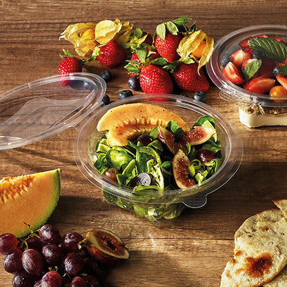 Un bol à salade et à charcuterie Starpak 50 avec couvercle rabattable, R-PET transparent rond, contient une salade de melon et figues sur une table en bois avec des fraises, raisins, pain, cerises et fruits. Un autre conteneur Starpak R-PET avec des fruits est à proximité.