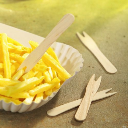 Ein Serviertablett mit goldbraunen Pommes Frites wird von umweltfreundlichen PAPSTAR „pure“ Birkenholzgabeln der PAPSTAR GmbH begleitet. Zwei weitere PAPSTAR „pure“ Pommes-Frites-Gabeln, Holz 8,5 cm, liegen auf der Ablage daneben. Die Szene ist auf einem hellen Hintergrund mit einem warmen, sonnigen Farbton gehalten.