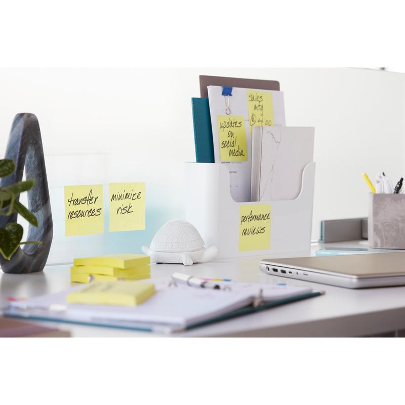 Een moderne bureautafel met een 3M Post-it® Super Sticky Notes-blok (76 mm x 76 mm, 90 vel, 100% PEFC) op een glazen scheidingswand, een schildpadfiguur, mappen in een documentenhouder, een gesloten laptop, pennen en een notitieboek.
