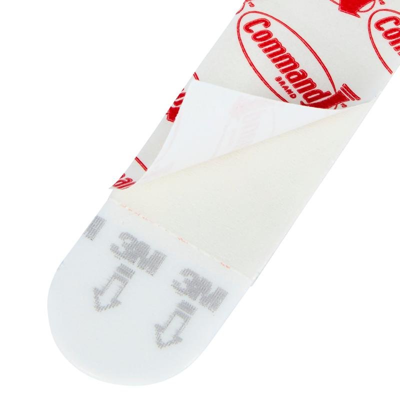 Een close-up van een Multipack Command™ Strips, 17200 van 3M Deutschland GmbH met gedeeltelijk verwijderde beschermfolie, die het kleefoppervlak en de gedrukte instructies voor het ophangen van foto's - de perfecte kleefstrips zonder boren - toont.