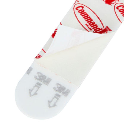 Een close-up van een Multipack Command™ Strips, 17200 van 3M Deutschland GmbH met gedeeltelijk verwijderde beschermfolie, die het kleefoppervlak en de gedrukte instructies voor het ophangen van foto's - de perfecte kleefstrips zonder boren - toont.