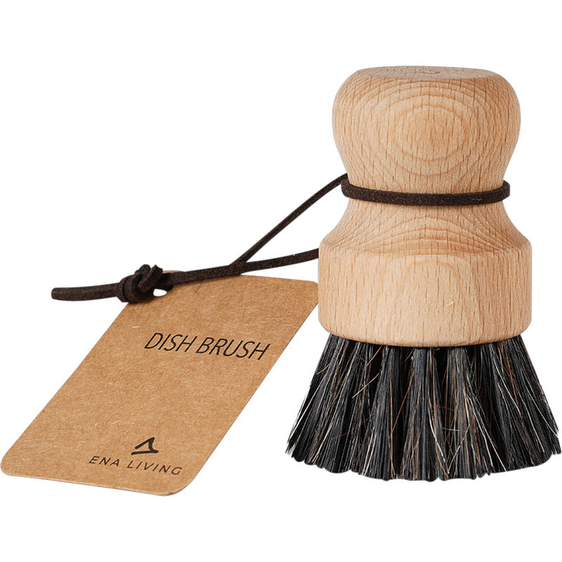 La brosse à vaisselle ENA Living avec des poils doux de Abena Re-Seller GmbH a une tête en bois ronde, un manche court, une boucle en cuir et une étiquette "DISH BRUSH" - idéale pour un nettoyage doux de la cuisine. Disponible dans une boîte de 12 paquets.