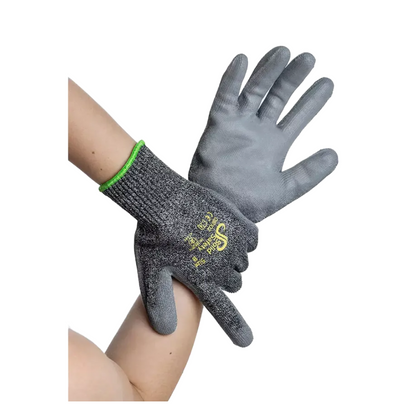 Deux mains portent des gants de protection contre les coupures AMPri SolidSafety Cut High, des gants de travail gris en matériau résistant aux coupures. Ces gants de la société AMPri Handelsgesellschaft mbH présentent une surface texturée avec un texte jaune-blanc au dos et ont un bord vert au poignet, offrant à la fois durabilité et protection.