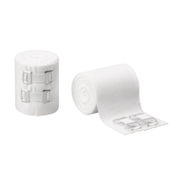 Op de afbeelding zijn twee rollen te zien B. Braun Askina® Ideal DIN-idealbinde van B. Braun Deutschland GmbH & Co. KG. De ene rol is stevig omwikkeld met metalen klemmen, terwijl de andere gedeeltelijk is afgerold en het gestructureerde, huidvriendelijke katoenen oppervlak zichtbaar maakt. Daarnaast liggen twee afzonderlijke metalen klemmen, dit alles tegen een eenvoudige witte achtergrond.
