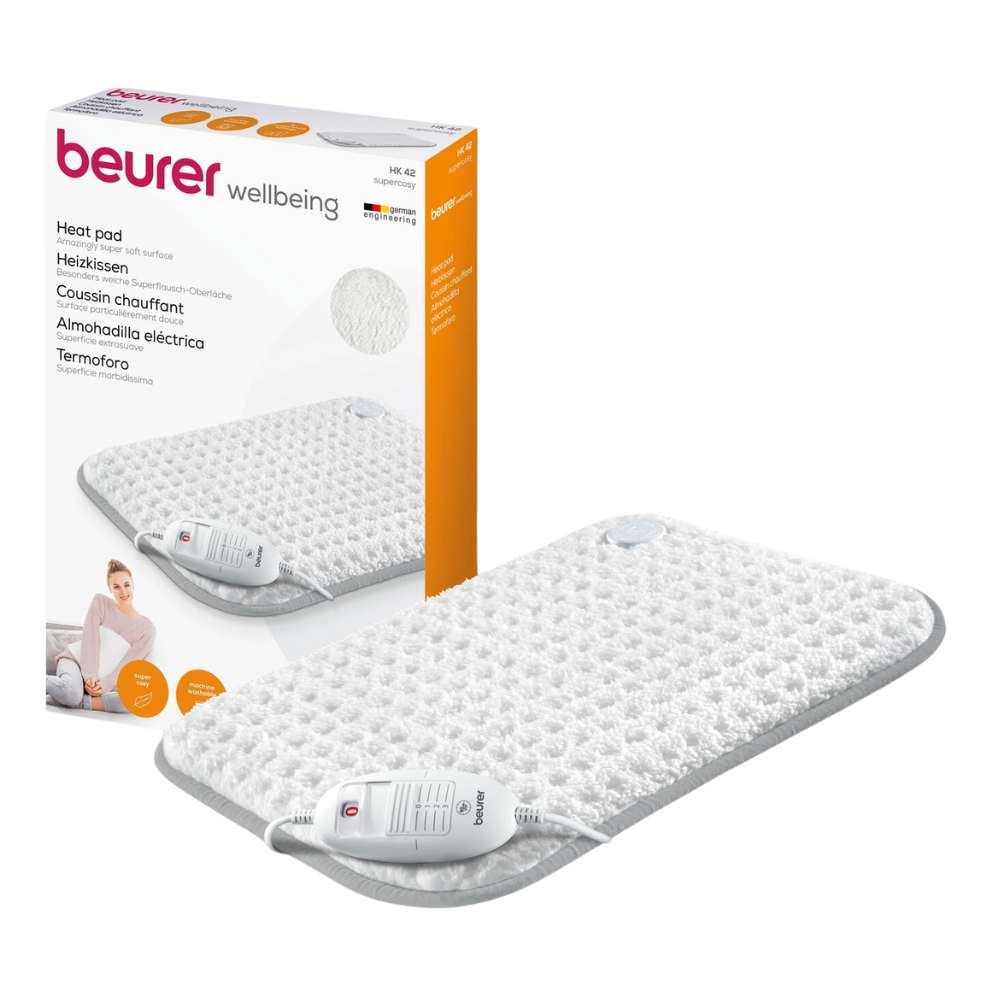 Naast het product is een Beurer HK 42 verwarmingskussen Super-Cosy van de Beurer GmbH met het merk 'wellbeing' op de verpakking afgebeeld. Het witte kussen met grijze rand is uitgerust met een afstandsbediening. De verpakking toont bovendien een afbeelding van het verwarmingskussen in gebruik en benadrukt de snelverwarmingsfunctie.