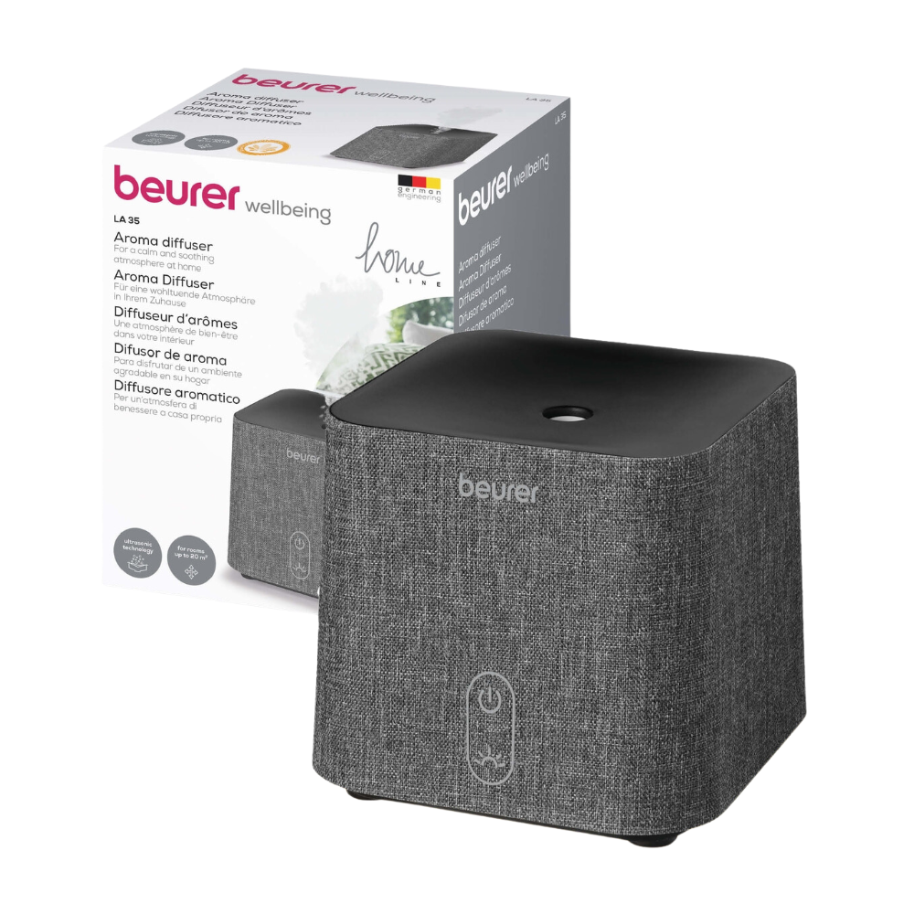 Afbeelding van een Beurer LA 35 aroma-diffuser voor zijn verpakkingsdoos. De diffuser van Beurer GmbH is grijs met een stofstructuur en heeft een enkele bedieningsknop aan de voorkant. Hij gebruikt ultrasone verneveling voor een effectieve verstuiving en op de doos staan dezelfde diffuser, productnaam en details in meerdere talen afgebeeld.