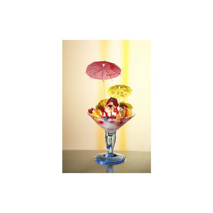 In een glazen beker bevindt zich een kleurrijke ijscoupe, versierd met bollen van kersen, gesneden fruit en kleurrijke PAPSTAR deco-prikkers van de PAPSTAR GmbH. De zacht verlichte achtergrond laat het dessert optimaal tot zijn recht komen.